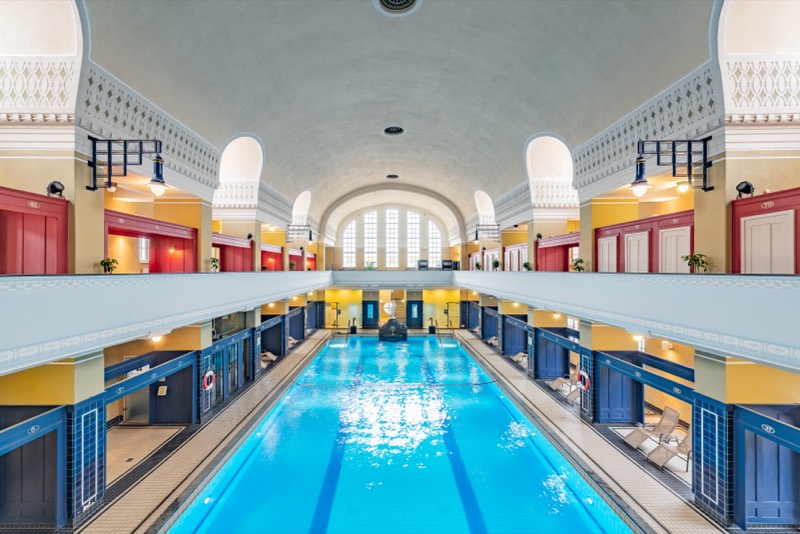 Schwimmhalle des Jugendstilbads Darmstadt mit türkisblauem Becken, Galerien und gewölbter Decke