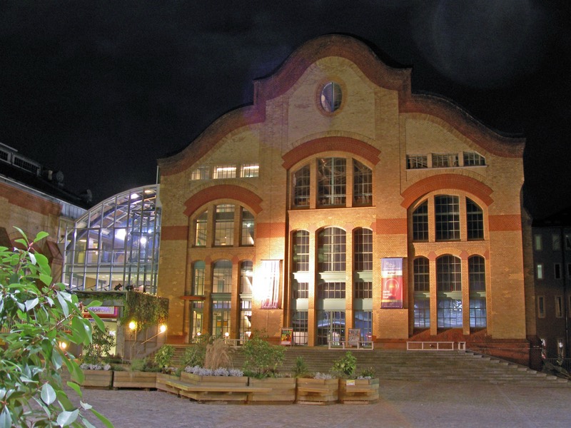 Die Centralstation in Darmstadt bei Nacht: beleuchtete Backsteinfassade der ehemaligen Industriehalle mit Rundbogenfenstern