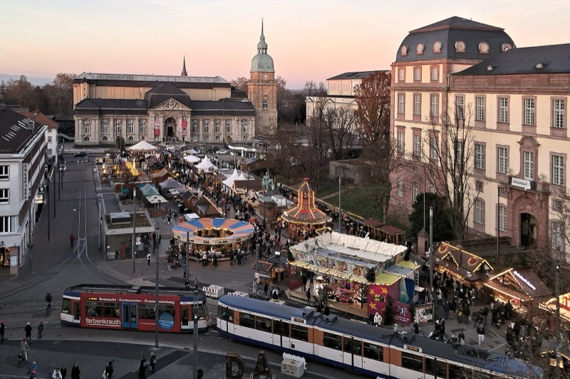 Weihnachtsmarkt auf dem Darmstädter Friedensplatz in der Abenddämmerung mit Karussells und Buden, dahinter das Hessische Landesmuseum, rechts das Residenzschloss