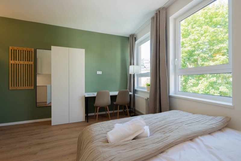 Studio 3 – Bett vor grüner Wand mit Arbeitsplatz