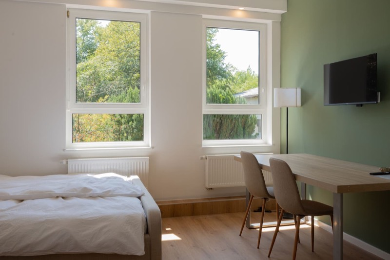 Studio 4 – Bett mit Esstisch und TV vor grüner Wand